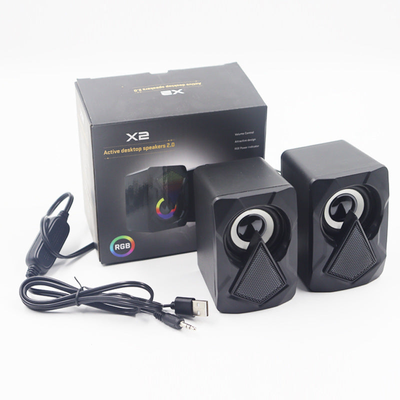 Black computer speakers with RGB lighting and USB cable next to their packaging on a white background