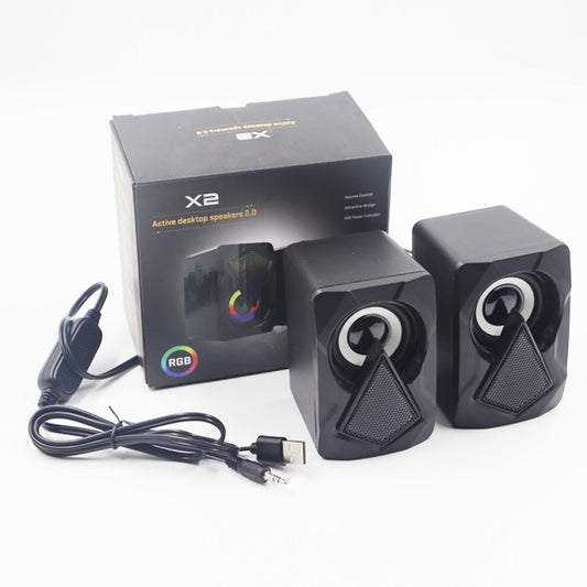Black computer speakers with RGB lighting and USB cable next to their packaging on a white background