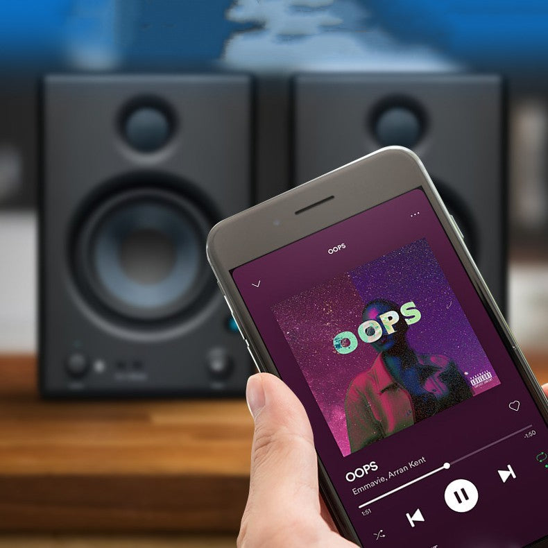 Hand holding a smartphone with music app on screen in front of speakers